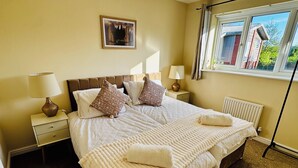 Un letto ben rifatto con copripiumino e cuscini a fantasia, una lampada da comodino, un quadro appeso alla parete e una finestra con vista sugli edifici.