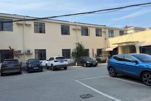 A parking lot with several cars parked in front of a building with multiple windows and air conditioning units. - Lexin Business Hotel (Wuxi)