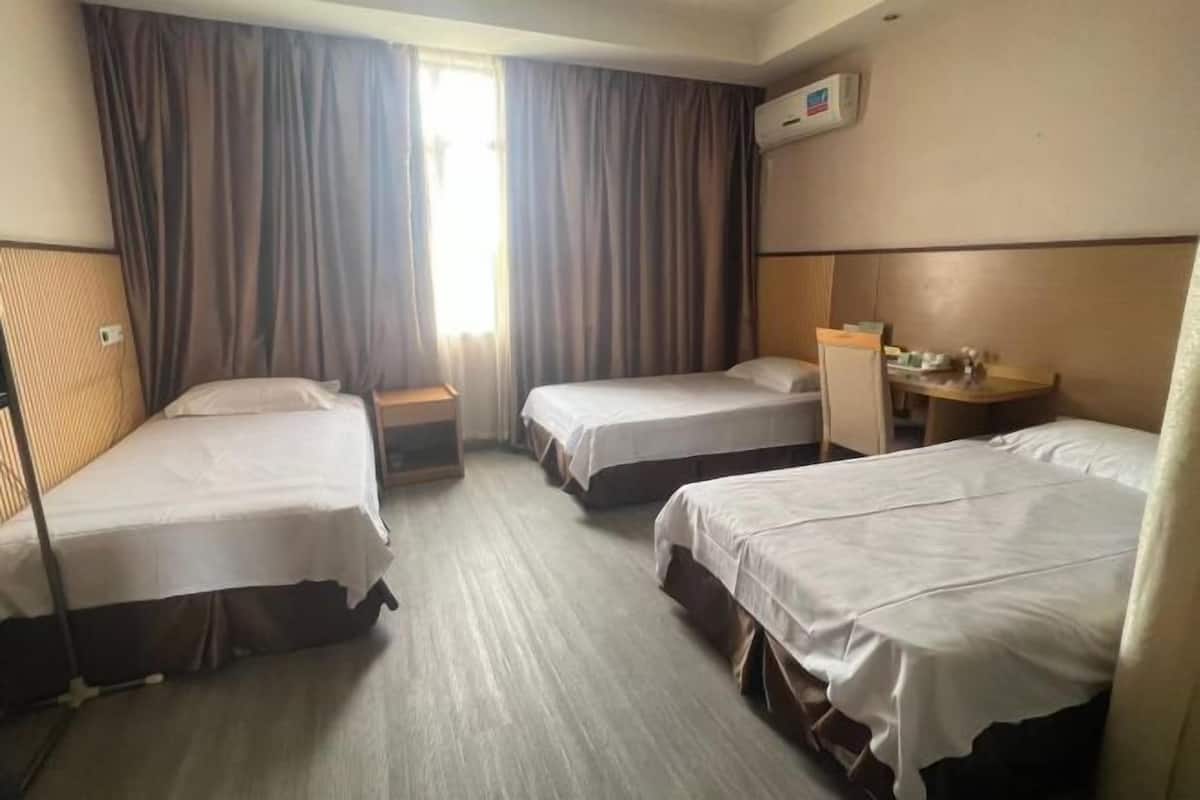 A hotel room with three single beds, a small table, and a chair.