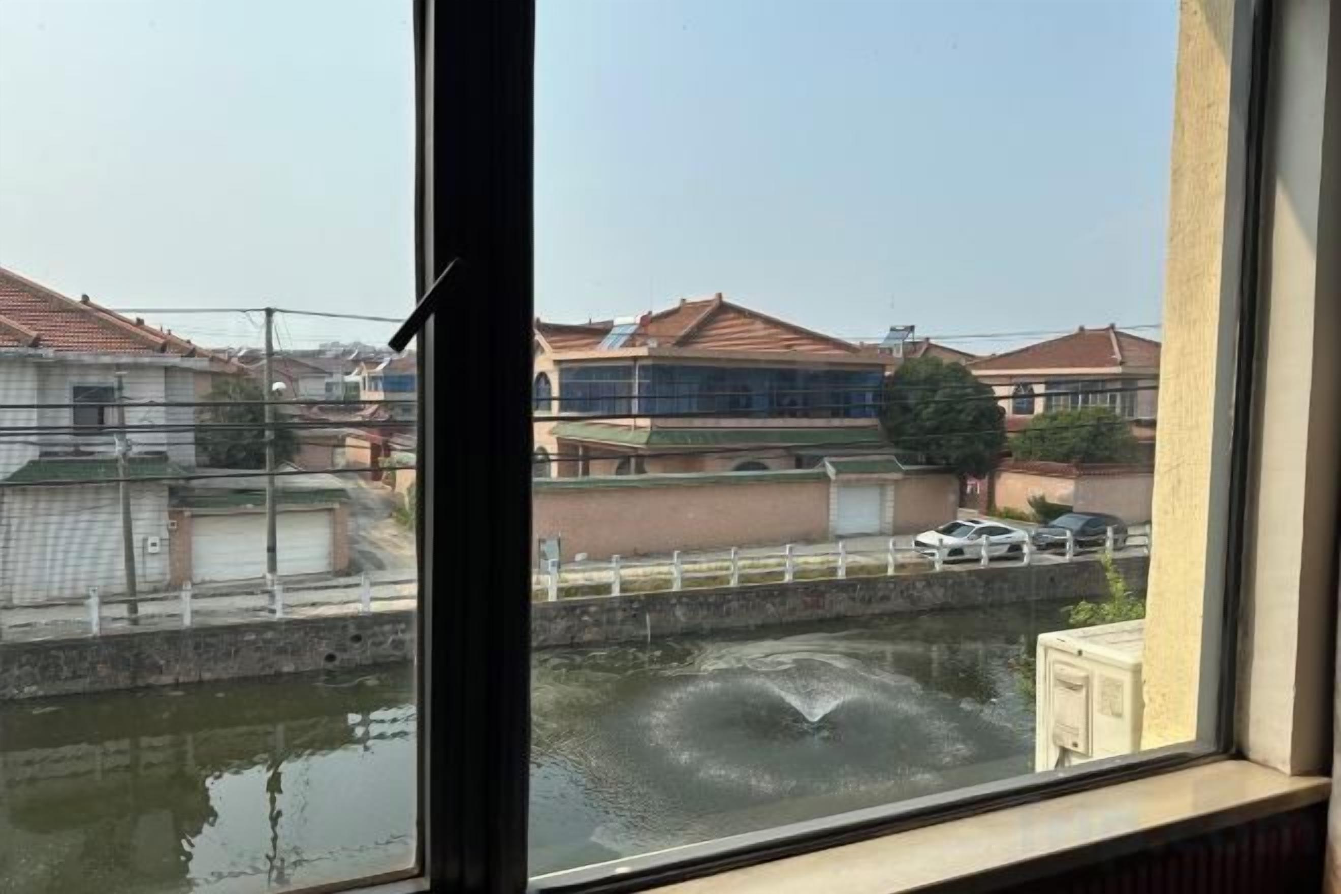 Blick durch ein Fenster auf ein Gewässer mit Gebäuden im Hintergrund.