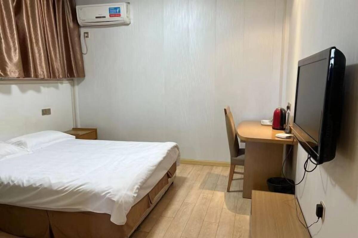 A hotel room with a bed, a desk with a chair, a television, and a small table.
