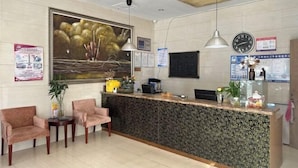 A reception area with a reception desk, two chairs, a clock, and a large painting on the wall. - Lexin Business Hotel (Wuxi)
