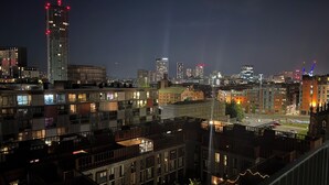 A nighttime cityscape with modern buildings, a mix of residential and commercial structures, and a prominent high-rise with red lights. - Luxury Manchester City Centre Apartment (Manchester)