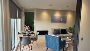 A modern living room with a sofa, a dining table with chairs, and a large window. - Luxury Manchester City Centre Apartment (Manchester)