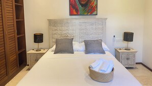 Ein Schlafzimmer mit einem großen Bett, zwei Nachttischen, einem Kopfteil mit Fischreliefs, einem Gemälde über dem Bett und einem Kleiderschrank mit Schiebetüren.