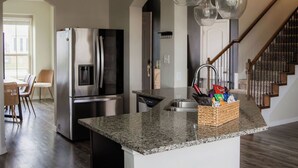 Une cuisine moderne dotée de plans de travail en granit, d’appareils électroménagers en acier inoxydable et de luminaires suspendus.