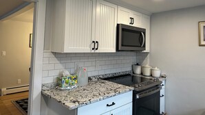 A kitchen with white cabinets, a microwave, a stove, and a countertop with a dish soap bottle and a tissue box. - End of season price drop! Sandwich recent renovate, single house, close to beach (Sandwich)