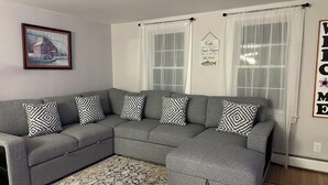 A grey sectional sofa with patterned cushions, a framed picture on the wall, and a rug on the floor. - End of season price drop! Sandwich recent renovate, single house, close to beach (Sandwich)