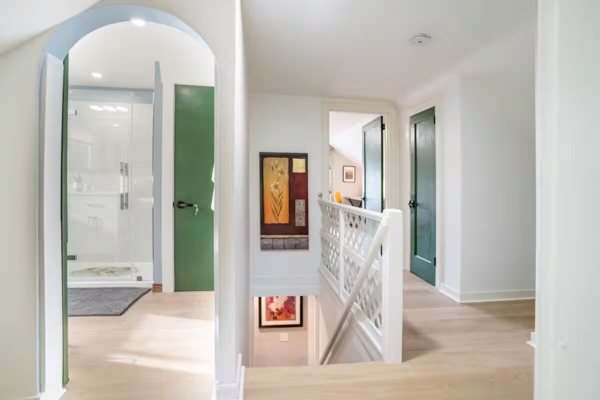 A modern interior with a staircase leading to a lower level, a door with a decorative panel, and a view of a hallway.