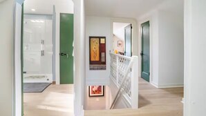 Ein modernes Interieur mit einer Treppe, die zu einer niedrigeren Ebene führt, einer Tür mit dekorativer Verkleidung und Blick auf einen Flur.