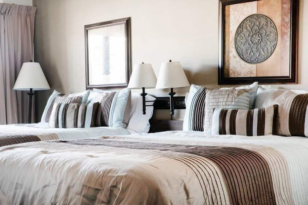 A hotel room with a large bed, two bedside tables with lamps, a framed picture on the wall, and a decorative wall piece.