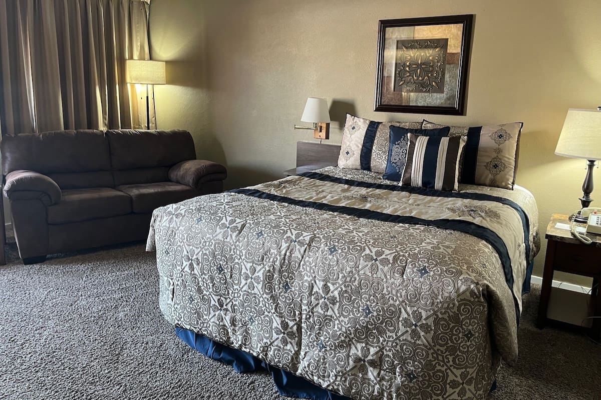 A hotel room with a large bed, a sofa, a bedside table with a lamp, and a framed picture on the wall.