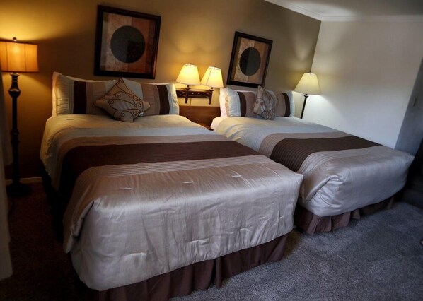 A hotel room with two beds, each with a headboard, a nightstand with a lamp, and two wall-mounted lamps. - Marcus Daly Motel (Anaconda)