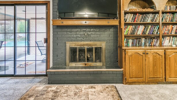 A living room with a fireplace, a bookshelf, and a large window overlooking a pool. - Spacious 5-bedroom house with AC, WiFi in phenomenal Oklahoma City (Oklahoma City)