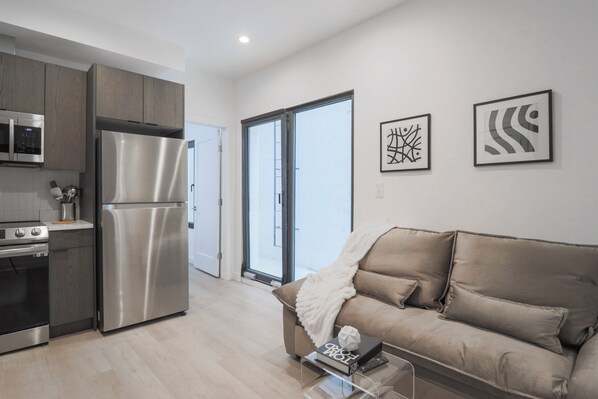 A modern kitchen with stainless steel appliances, a sofa, and artwork on the wall. - Unit 2: Cozy 1-Bed in the heart of Dc (Washington)