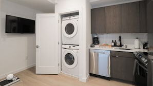 A compact kitchen with a washing machine, dishwasher, and a flat-screen TV mounted on the wall. - Unit 2: Cozy 1-Bed in the heart of Dc (Washington)
