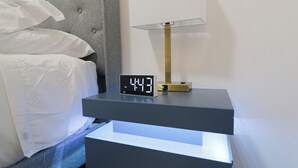 A modern bed with white linens, a digital clock, and a bedside table with a lamp. - Unit 6: Studio /Queen +Sofa Bed in the heart of DC (Washington)