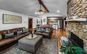 A living room with a brown leather sofa, a grey ottoman, a patterned rug, and a stone fireplace. - Mountain View Woodland Respite|Hot Tub & Arcade & Pool (Sevier County)