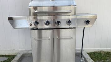 A stainless steel outdoor grill with four burners, a lid, and a side shelf.