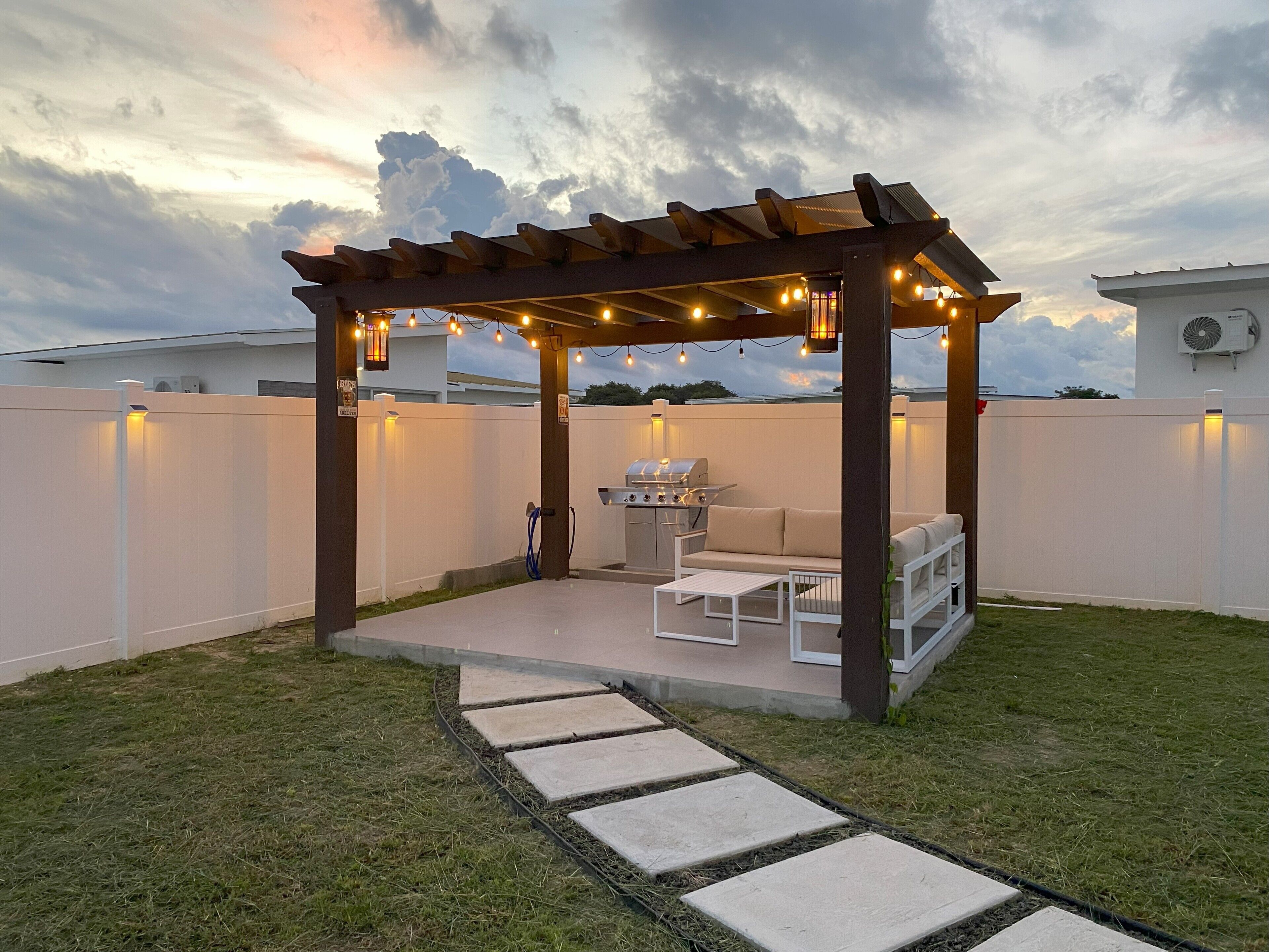 Ein überdachter Patio-Bereich mit Grill, Sitzgelegenheit und Lichterketten.