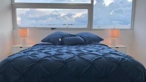Une chambre à coucher avec un grand lit, deux lampes de chevet et une fenêtre donnant sur le ciel et les nuages.