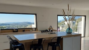 A modern kitchen with a large island, bar stools, and large windows offering a view of the landscape.