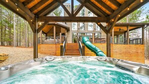 Un jacuzzi con tobogán que da a una terraza de madera, rodeado de árboles.