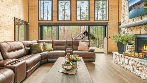 Una sala de estar acogedora con un sofá de cuero, chimenea y ventanas amplias con vistas al bosque.