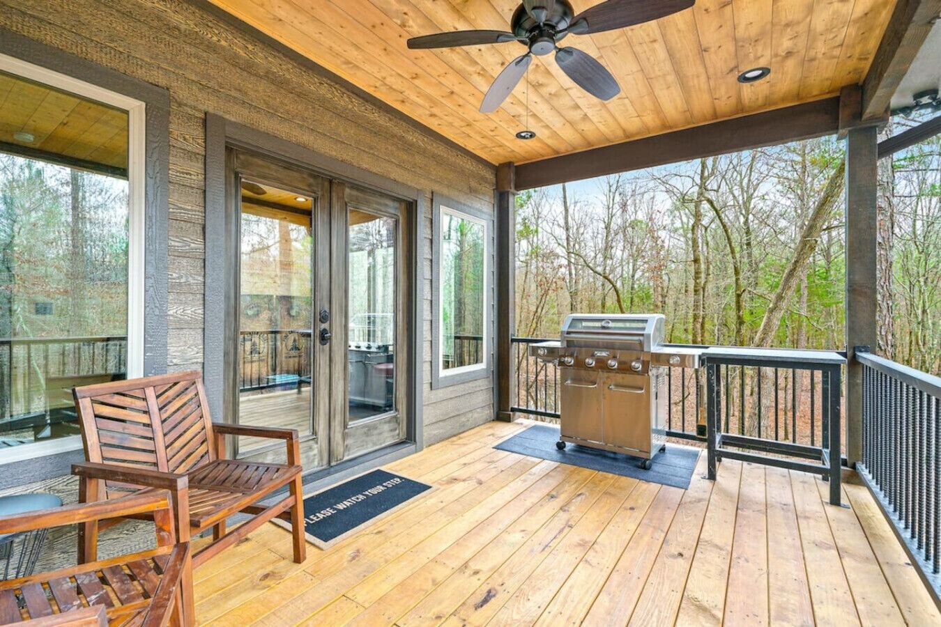 A covered deck with a grill, a chair, and a view of the surrounding trees.