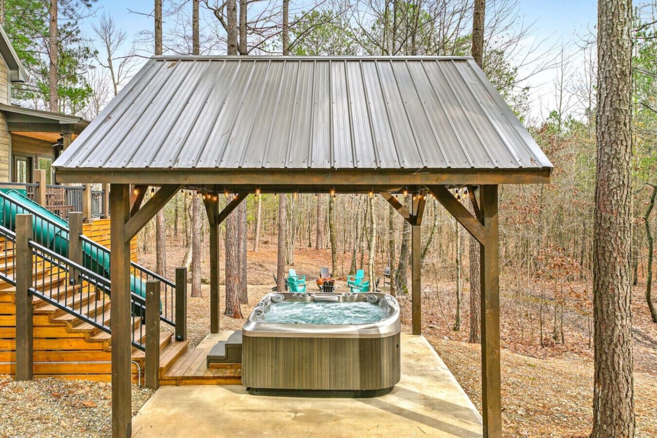 A hot tub under a wooden gazebo in a forested area.