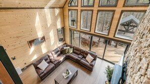 Amplia sala de estar con un sofá de cuero en forma de L, una mesa de centro y vistas a una terraza exterior con una mesa y sillas de comedor.