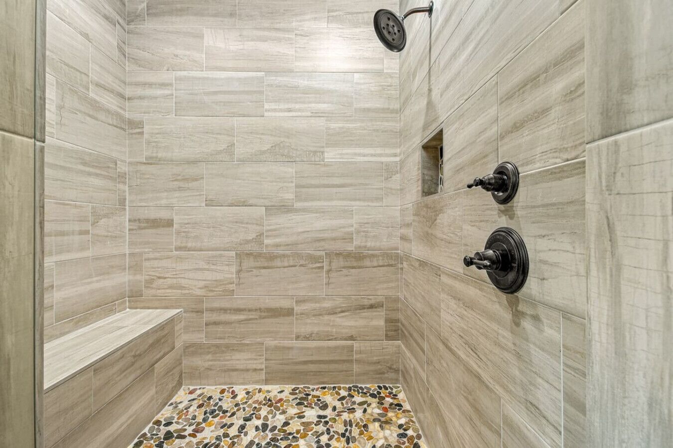 A shower with a pebble-patterned floor, tiled walls, and a handheld showerhead.