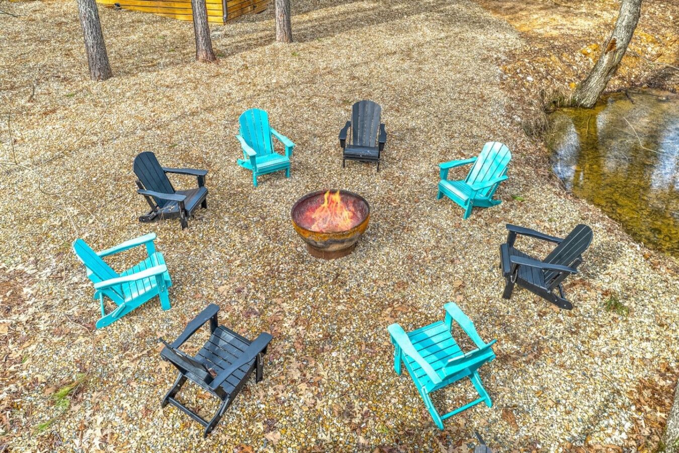 Un ensemble de chaises Adirondack disposées en cercle autour d’un foyer central, le tout sur une surface recouverte de gravier.