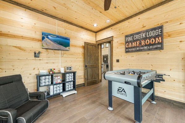 A Pine Creek Lodge game room with a foosball table, a TV mounted on the wall, and a cozy seating area.