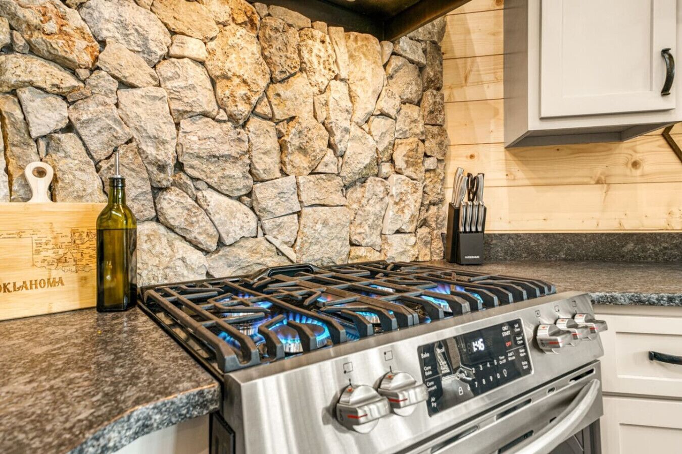 Una cocina con pared de piedra, estufa a gas y tabla de madera con una botella.
