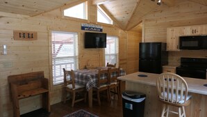 Ein Holzblockhaus-Interieur mit Esstisch, Stühlen, einem Fernseher, einem Kühlschrank und einer Mikrowelle.