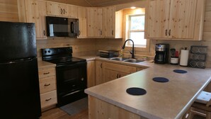 Eine Küche mit Holzausstattung, einem schwarzen Kühlschrank, einer Mikrowelle, einem Herd, einem Spülbecken und einer Kaffeemaschine.