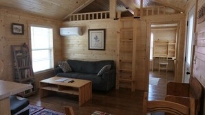 Ein gemütliches Blockhaus-Interieur mit Holzboden, einer Couch, einem Couchtisch, einem Bücherregal und einem Etagenbett.