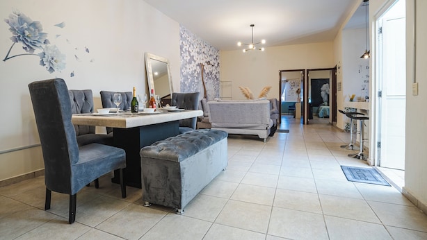 Un salon moderne avec un coin repas, comprenant un canapé, des fauteuils, une table basse et un grand miroir.