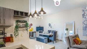 Une cuisine moderne avec un coin repas, comprenant des luminaires suspendus, un téléviseur et un canapé agrémenté d’un miroir.