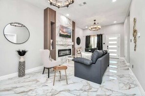 Un salon moderne avec un canapé gris, un miroir rond, un vase et une cheminée.