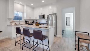 Una cocina moderna con armarios blancos, electrodomésticos de acero inoxidable y una isla central con taburetes de bar.