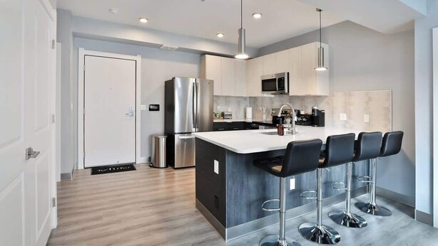 A modern kitchen with a central island, stainless steel appliances, and bar stools.