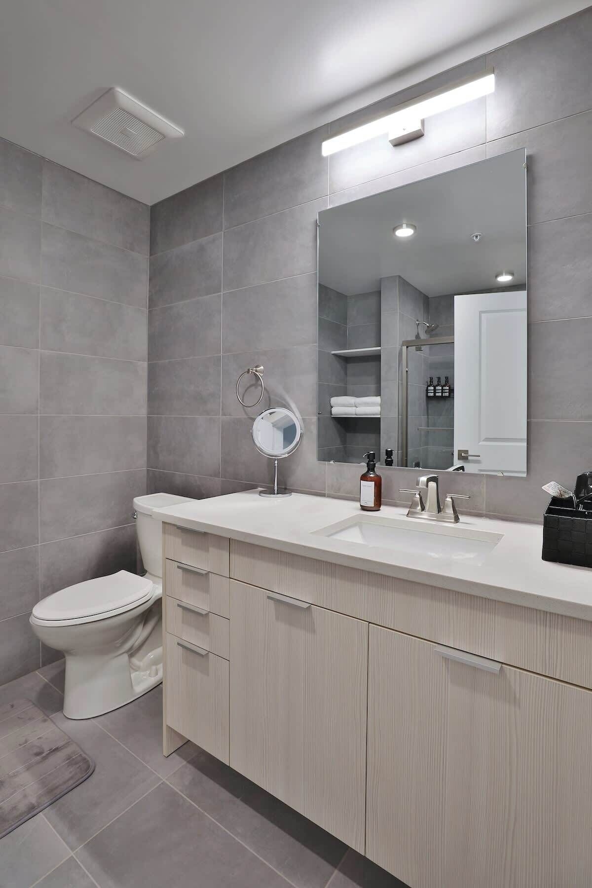 A modern bathroom with a toilet, sink, mirror, and cabinet.