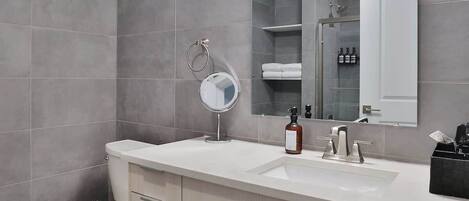 A modern bathroom with a toilet, sink, mirror, and cabinet.