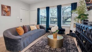 A modern living room with a curved grey sofa, a round coffee table with a vase, and a black and white patterned rug.