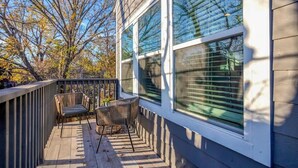 A wooden deck with two chairs and a table, overlooking a backyard with trees and a house.