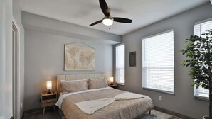 A bedroom with a bed, a ceiling fan, bedside lamps, a world map on the wall, and a potted plant. - Home Away from Home Near Downtown (Columbus)