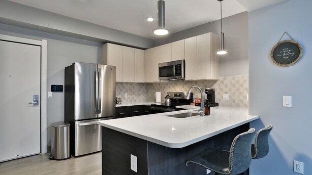 A modern kitchen with stainless steel appliances, a white countertop, and bar stools. - Home Away from Home Near Downtown (Columbus)