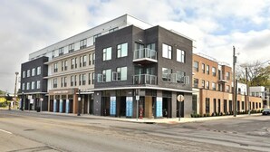 A multi-story building with a modern architectural design, featuring a mix of brick and glass facades, and a ground-level commercial space with signage. - Home Away from Home Near Downtown (Columbus)